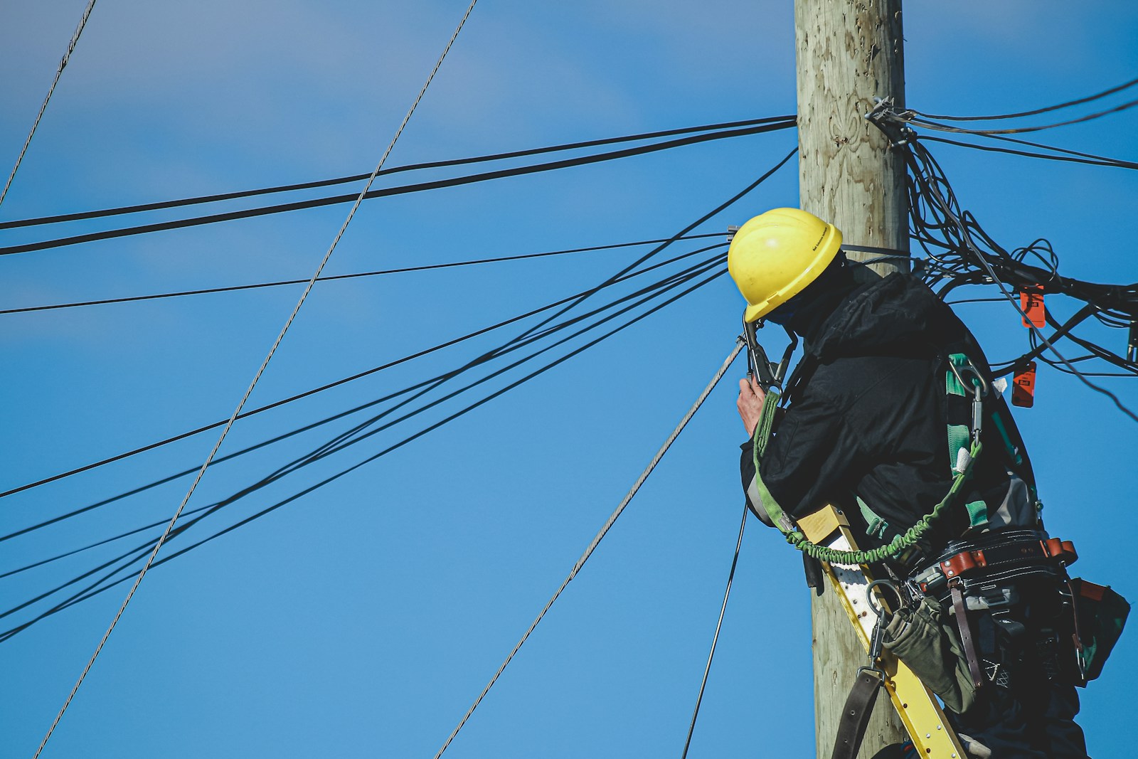 Servicios Asenov Telecomunicaciones Cox - man in black jacket and yellow hard hat climbing on brown wooden post during daytime